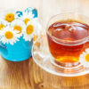 Chamomile tea in a glass cup and chamomile flowers in a small blue watering can